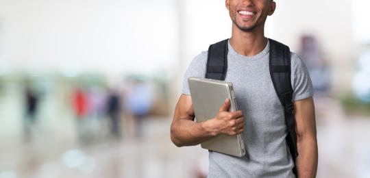 Menino negro segurando um notebook, com uma mochila nas costas