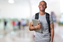 Menino negro segurando um notebook, com uma mochila nas costas